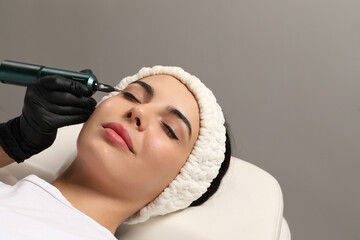 Young woman undergoing procedure of permanent eyeliner makeup on grey background, closeup - obrazy, fototapety, plakaty