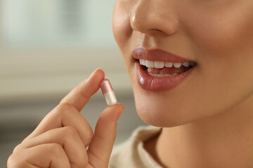 Young woman taking dietary supplement pill on blurred background, closeup