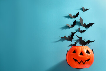 Flat lay composition with paper bats and plastic pumpkin basket on light blue background, space for text. Halloween decor