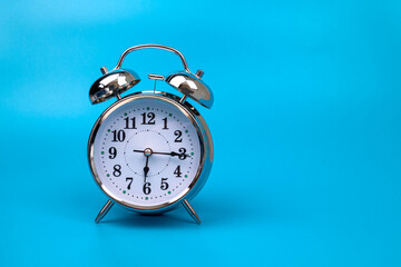 silver vintage alarm clock falls on the floor with a blue background