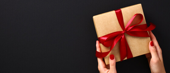 Female hands with luxury gift box on black background. Black friday sale banner design. Flat lay, top view, copy space.