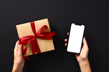 Female hands with luxury gift box and smartphone mockup with blank screen. Black Friday sale...
