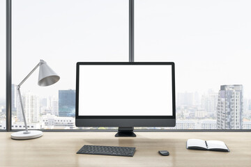 Close up of blank white computer monitor on wooden office desktop with objects, lamp and supplies on panoramic window and city view background. Mock up, 3D Rendering.