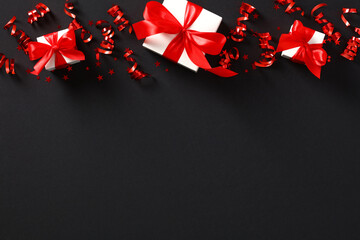 Red party streamers, gift boxes, confetti on black background. Black Friday, Christmas, New Year...