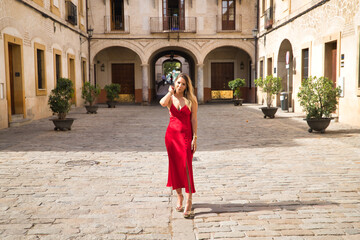 Fototapeta na wymiar Young, attractive, blonde woman in an elegant red party dress touching her hair while strolling through the city. Concept beauty, fashion, elegance, luxury.