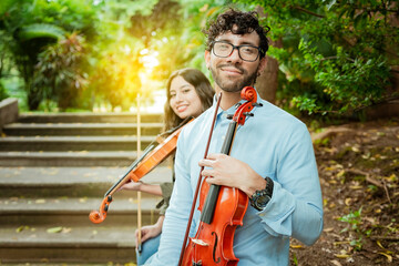 Portrait of two young violists sitting outside. Man and woman violinist sitting on the stairs....