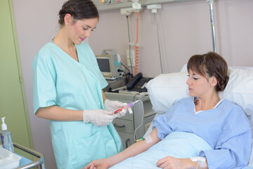 nurse taking blood sample from patient in hospital bed