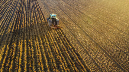 aerial view of farmer driving tractor deep plowing land at sunset, Piacenza, Italy 