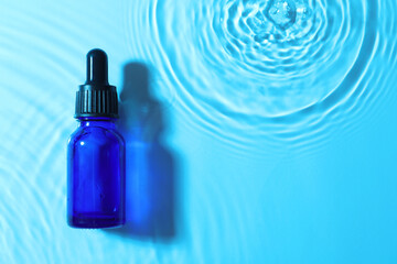 Fototapeta Bottle of face serum in water on light blue background, top view. Space for text obraz
