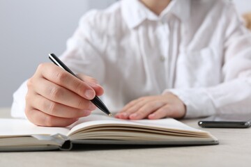 Woman writing in notebook at wooden table in office, closeup