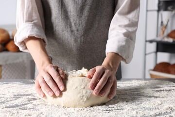 Woman kneading dough at table in kitchen, closeup