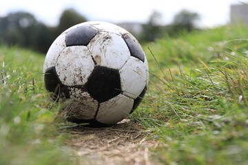 Dirty soccer ball on green grass outdoors, space for text