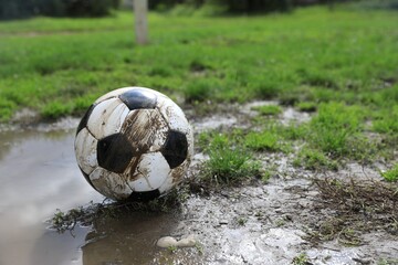 Dirty soccer ball on green grass near puddle outdoors, space for text