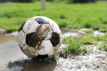 Dirty soccer ball on green grass near puddle outdoors, space for text