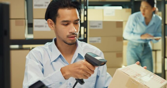 Close-up Asia man and girl partner wear formal shirt sit front desk computer use barcode machine scan record customer online data in cardboard box deliver at warehouse. Startup small business concept.