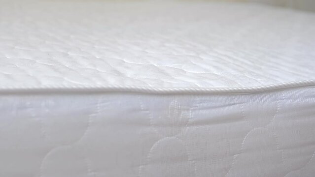 Close up of a girl's hand checks the rigidity of a new comfortable orthopedic white mattress for the bed. Female hand pressed on orthopedic surface. Girl tests elasticity softness orthopedic mattress.