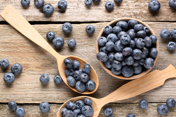 Spoons and bowl with tasty fresh blueberries on wooden table, flat lay - Powered by Adobe