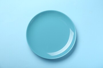 Empty ceramic plate on light blue background, top view