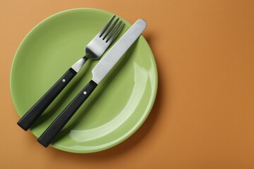 Green ceramic plate with cutlery on pale orange background, top view. Space for text