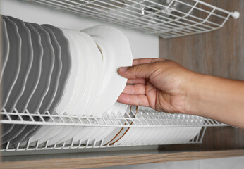 Woman taking ceramic plate from drying rack in kitchen, closeup