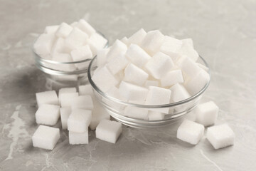 Bowls with sugar cubes on grey marble table, closeup