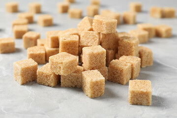Heap of brown sugar cubes on light grey marble table, closeup
