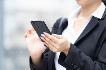 屋外でスマートフォンを使うスーツ姿の若い女性