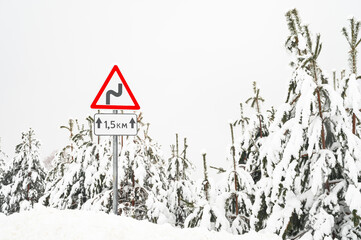 Winter road trip concept. View through the windshield of a car at a warning road sign. Driving on a snowy country road.