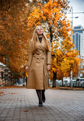 portrait of blonde woman in beige coat walking on the street  in the Kyiv city in autumn park