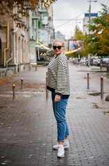 Fototapeta na wymiar smiling woman with long blond hair in sunglasses and blue jeans walking on the street
