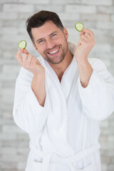man at spa wearing robe holding cucumber slice