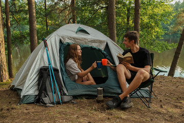 Portrait of couple of travelers dating in forest trip with tent and book in summertime.