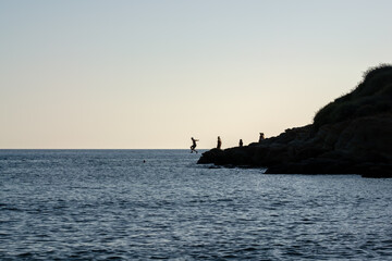 Tourists jumping of a cliff at the Mylopotas beach in Ios Greece