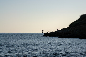 Obraz premium Tourists jumping of a cliff at the Mylopotas beach in Ios Greece