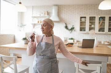 Female in the apron sipping a beverage in the kitchen