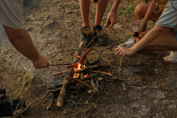 Shot of three travelers friends roasting sausages on bonfire in woods.