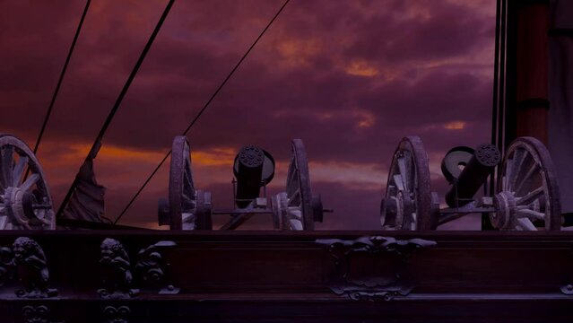 A close-up view of an old wooden battleship sailing past at dawn with rotary cannon guns lined up on the upper deck ready for battle.