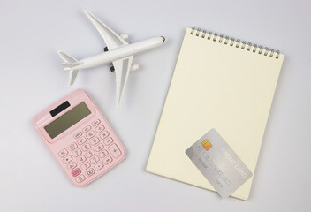 flat lay of pink calculator, airplane model, blank page opened note book and credit card on white background. traveling planing budget concept.