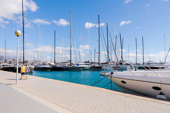 Pareja paseando por el Paseo Mar&iacute;timo de Palma de Mallorca, junto a un puerto deportivo con yates y veleros. Mallorca, Islas Baleares, Espa&ntilde;a.