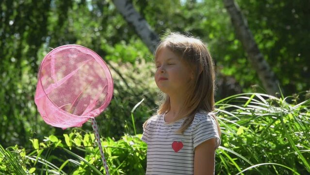 Cute girl with pink scoop net for hunting butterflies is looking at camera