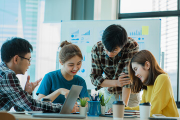 Asian creative teams sit and work together to share inspirational creativity in a workshop. Young modern businessmen are meeting with graph paper and laptop in the workplace.