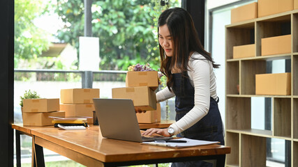 Startup small business owner using laptop computer to receive order from customer and prepare parcel box of product for delivery