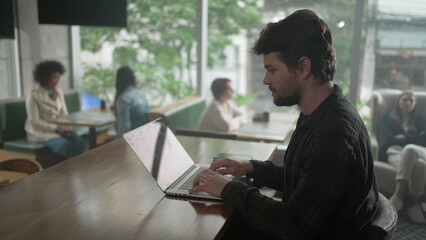 Entrepreneur in front of laptop at coffee shop. Young man freelancer using computer at cafe place