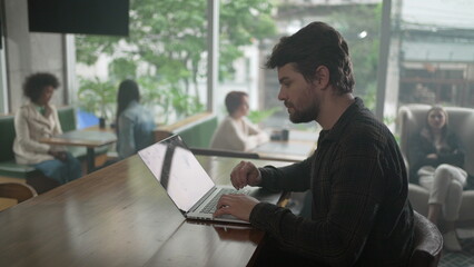 Entrepreneur in front of laptop at coffee shop. Young man freelancer using computer at cafe place
