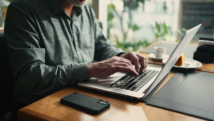 Closeup businessman hands typing on laptop keyboard working remotely at cafe place