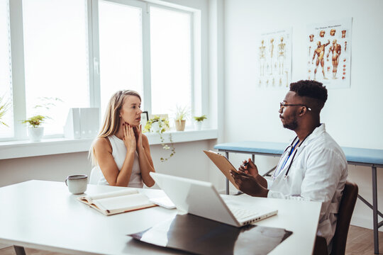 A woman sits across the table from her male nurse, who shows her various medications. Young woman have problem with sore throat or thyroid gland. Endocrinologist examining throat 