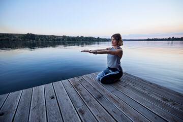Yogi woman meditates and does breathing exercises while sitting on the dock.