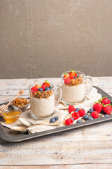 Granola with nuts, yogurt and red fruits berries in a jar. Breakfast parfait with muesli, yoghurt, red fruits berries and honey, white kitchen background.