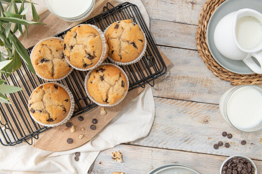 Chocolate chip muffins on a baking rack and glasses of milk on a white kitchen countertop.  Morning breakfast table. Top view, flat lay