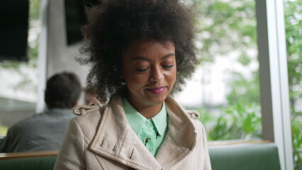 One happy black woman checking phone at coffee shop. Smiling African American girl with Afro hair reading cellphone message